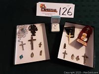 Overview of religious items including crucifixes, rosaries and pendants arranged in two white trays and necklace box.