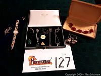 Overview of lot showing multiple necklaces, pendants, a watch, bracelet, rings, and earrings displayed on a table with catalog card.