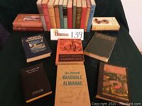 Photo showing multiple vintage hardcover books arranged, titles visible include American Government Handbook, How We Became Americans, and The Mutual Baseball Almanac.