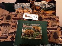 Wide shot showing the Italian velvet elk tapestry with large elk and mountains, along with three cabin-themed pillows including one with bear images and another with a stuffed small bear toy in a green pillow.