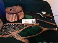 Wide shot of vintage fishing equipment showing rods with reels, creel, nets and bait box on dark surface