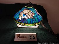 Stained glass lamp turned on, showing one fish design in beige and blue tones on a blue and green background with a yellow border.