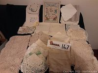 Full lot view of vintage linens including doilies, napkins, and cross stitch piece arranged on black background showing overall quantity and condition.