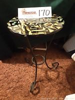 Side view of wrought iron side table showcasing round top with multi-colored iridescent mosaic and curved iron legs on brown carpet.