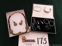 Full lot of jewelry displayed in boxes including green stone necklace with earrings and sterling silver jewelry set with bracelets, pendant, and various earrings.