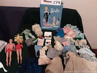Two vintage dolls and extensive collection of doll clothes spread out with a blue Barbie box behind them.