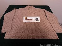 Full front view of the beige Aran Mor Merino wool sweater laid flat, showing cable knit pattern and ribbed hems.