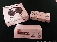 Two branded boxes: theBoom Quiet and theBoom side by side on dark cloth with lot card