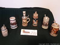 Photo of six decorative beer steins arranged in single row on dark fabric background