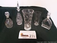 Photo showing all six items: two crystal vases and four crystal decanters, clear and etched with leaf motifs and patterns, with ground-stoppered decanters of different shapes and heights.