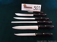 Six Cutco knives laid out in a row on green cloth background.