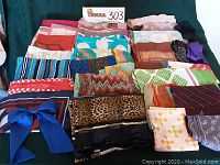 Overview of a variety of ladies scarves in different colors and patterns, arranged folded on a green surface.