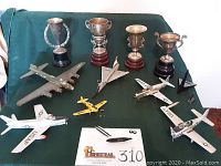 Full lot overview showing four silver trophies and seven model airplanes displayed on green cloth.