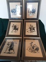 Six framed and matted black ink bullfighting sketches arranged on a dark green fabric background showing the varying poses of matadors and bulls, frames show wear and losses.