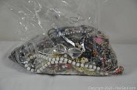 Large clear plastic bag filled with assorted necklaces showing white and pearl-like beads visible through plastic.