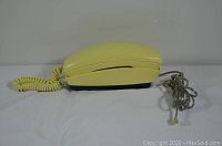 Side view showing the yellow phone and coiled receiver cord along with the attached cord ending in a modular plug.