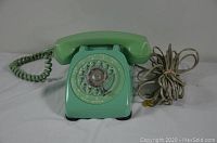 Front angle view of vintage turquoise rotary dial desktop phone showing handset, dial, coiled cord, and bundled connection cord