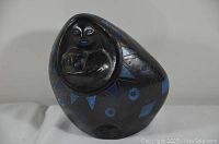 Front view of black pottery mother and child figure with blue geometric patterns on surface
