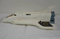 Side view of vintage Fisher Price space ship toy showing white plastic body, blue rocket thrusters, black wings with atomic symbol, and faded Fisher Price decal.