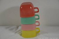 Stacked view of four retro glass cups in red, green, pink and yellow color.