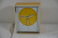 Front view of retro style portable Caravelle clock showing yellow circular face with metal wire hour markers, day and date display.