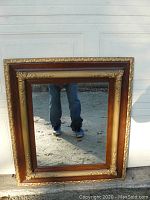 Full view of large rectangular mirror showing wooden frame with gold gesso ornamental detailing.