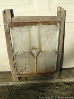 Front view of the tin ceiling panel in cedar fence board frame showing embossed diamond pattern and rust spots.