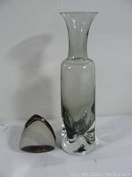 Clear thick glass vase with flared top and solid base, standing next to four stacked metal dishes.