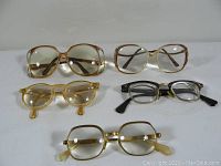 Top-down view of 5 pairs of vintage eyeglasses on white surface showing frame shapes and colors.