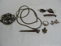 Overview photo showing all nine pieces in the lot on a white backdrop including buckle, necklace, earrings, brooches, ring, and comb.