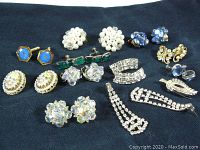 Photo showing a collection of vintage costume jewelry including cluster pearl earrings, rhinestone clip-ons, blue cufflinks, and faceted bead earrings on a dark fabric background