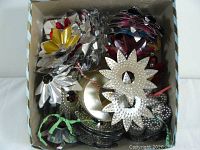 Box filled with assorted vintage Christmas light reflectors showing various colors and shapes including floral and geometric punched tin and foil designs.