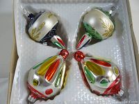 Full view of four vintage glass Christmas ornaments in original white cardboard packaging.