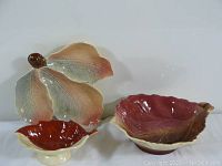 Three ceramic leaf-shaped dishes in different colors arranged together on a white surface