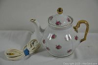 White ceramic electric teapot showing floral pink rose pattern, gold handle, lid handle, and attached electric cord