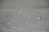 Clear cut crystal napkin holder with intricate floral and geometric cut designs, faceted edges, and a slanted rectangular shape on a white surface.