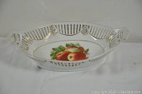 Front angle showing the oval pierced white ceramic dish with fruit painted in the center and gold accents around the edges and handles.