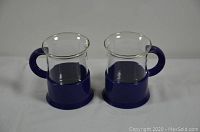 Two Bodum glass mugs with clear glass bodies and cobalt blue handles and bases placed side by side on a white surface.