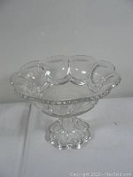 Clear pressed glass bowl with scalloped edges and pedestal base on a white background