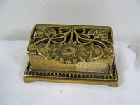 Closed view of brass stamp box showing lid with floral patterns and central flower detail.