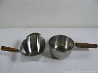 Photo of two small Danish stainless steel pots with teak wood handles, placed side by side to show size and design.
