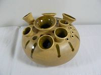 Side angle view showing the vase with nine varied openings around the circular body, tan exterior with drip glaze accents.