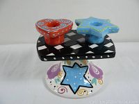 Front view of the candle holder showing colorful star and heart candle slots on a black and white checkerboard platform with a decorated base.