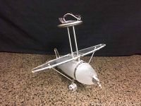 Front and side view of a glass airplane light fixture showing frosted glass fuselage and wings with silver metal frame and light fixture on top.