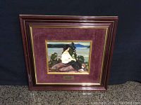 Framed painting with dark wooden frame and maroon velvet mat showing a woman sitting near water