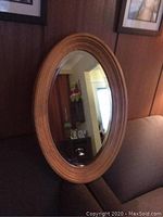 Full frontal view of oval mirror on a couch showing wood frame and reflection of room details