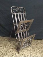 Foldable metal magazine rack with decorative scrollwork, shown in upright position on side view.