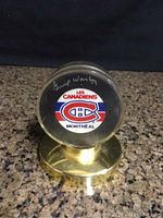 Front view of signed Montreal Canadiens hockey puck in clear case with gold-tone base showing signature and team logo.