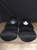 Two black car seats with Toronto Maple Leafs logos side by side displayed on floor with black backdrop.