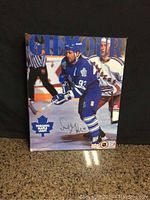 Full front image of signed Doug Gilmour hockey picture on board showing the player, signature, and two corners worn.